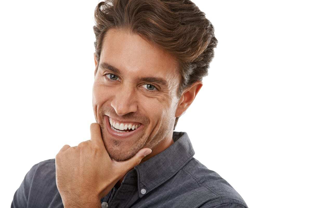 Smiling man with healthy white teeth touching his chin in a dental office setting.